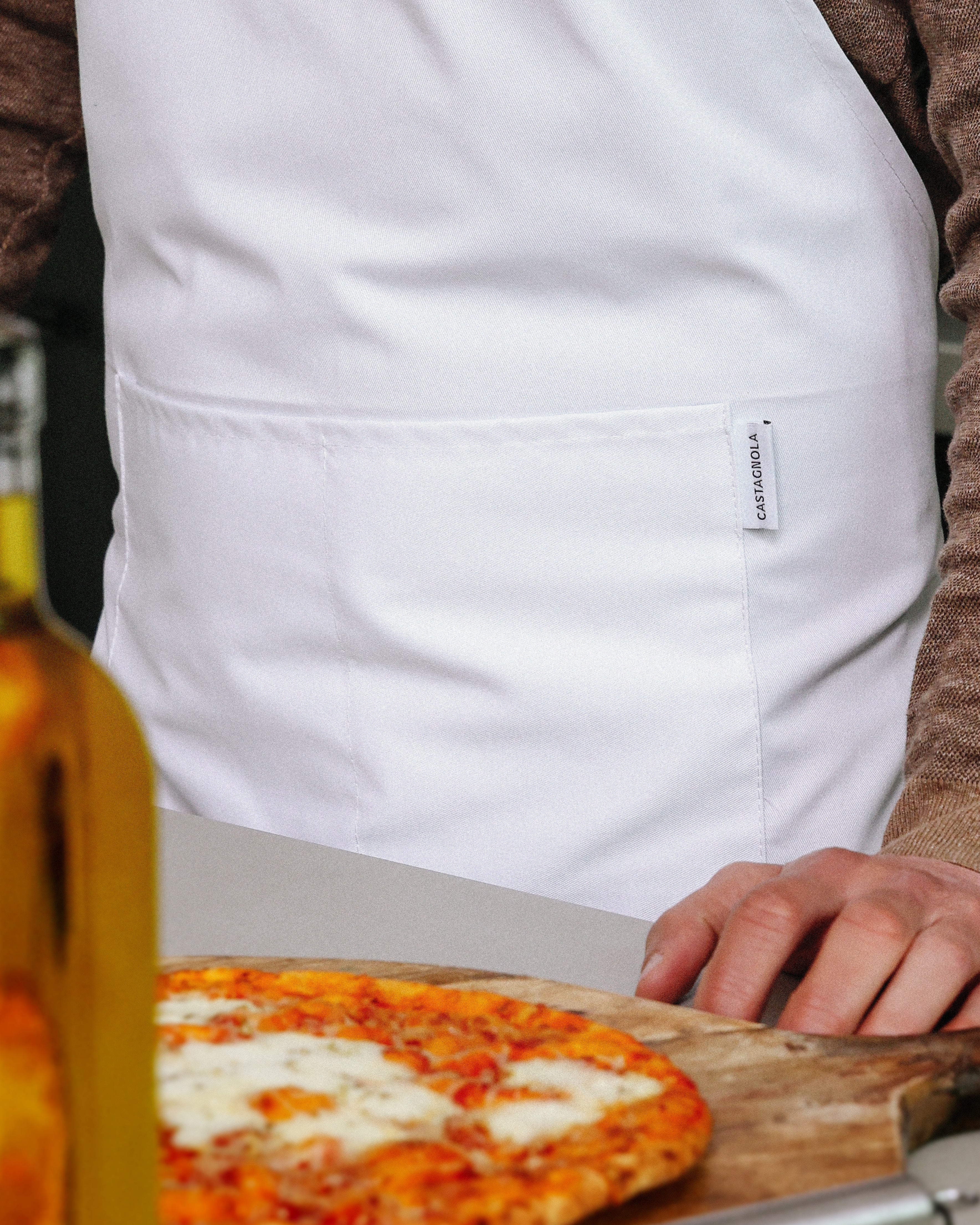 Man in keuken, in een Castagnola keukenschort, bereidt een pizza
